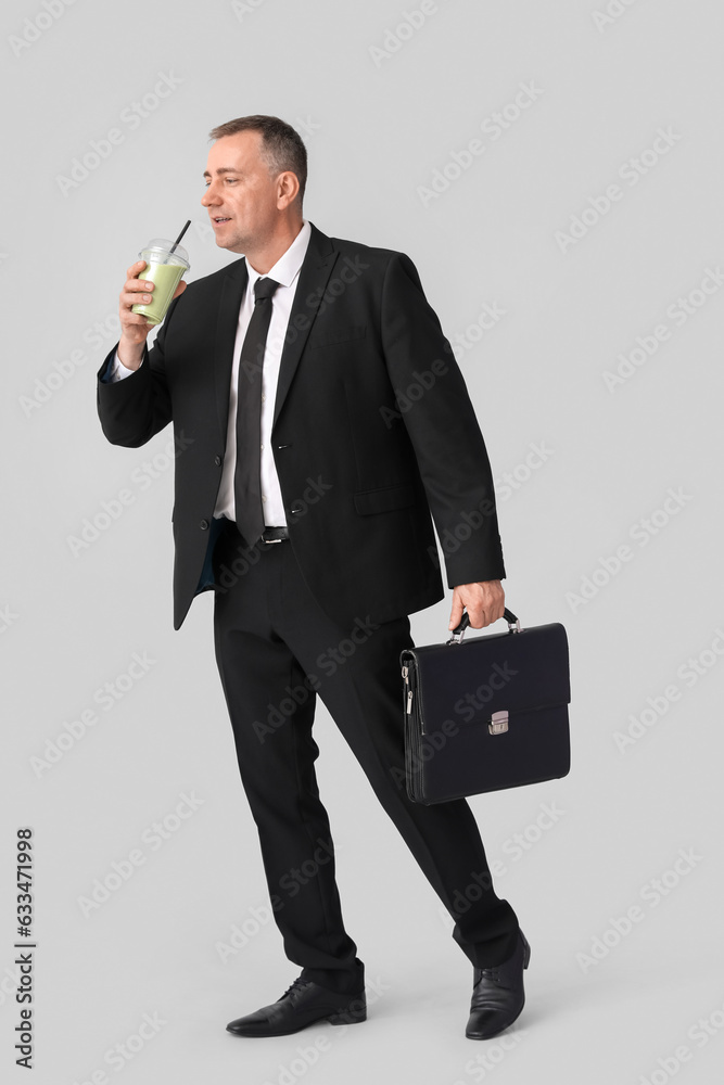 Mature businessman with glass of vegetable smoothie and briefcase on light background