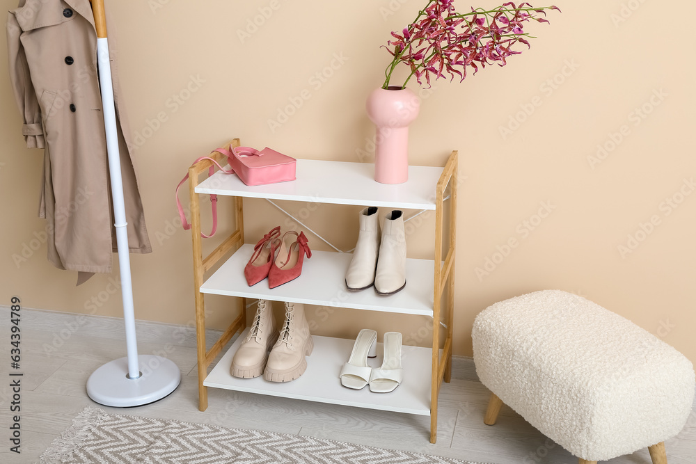 Shelving unit with shoes, bench and rack near beige wall in hall