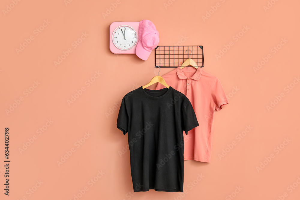 Stylish t-shirts and cap hanging on pink background