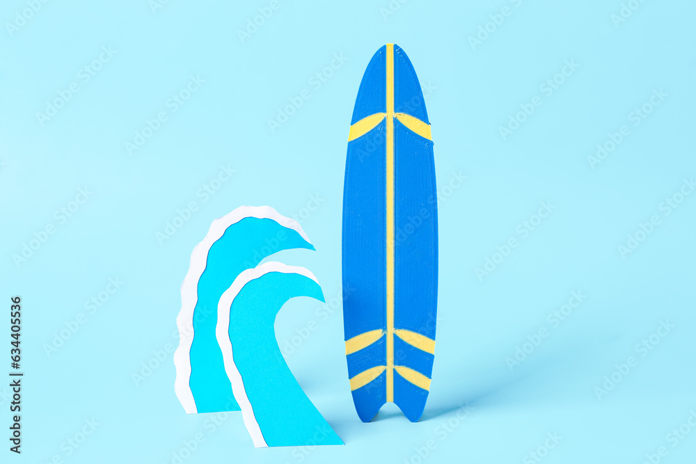 Creative composition with paper waves and mini surfboard on blue background