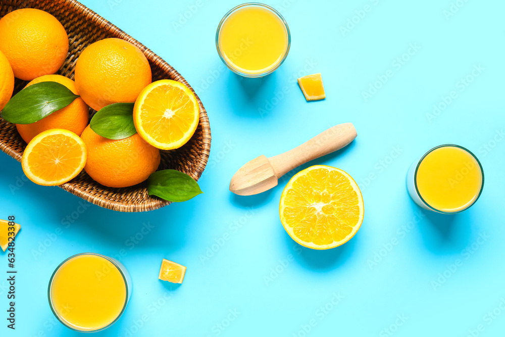 Glasses of fresh orange juice and wooden juicer on blue background