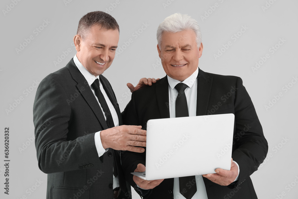 Mature brothers in suits using laptop on grey background