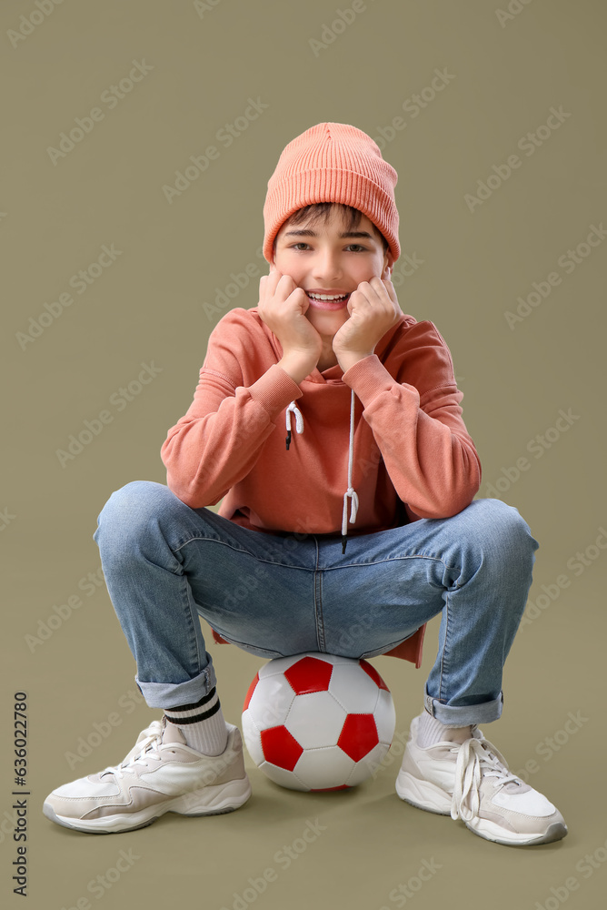 Little boy sitting on soccer ball against color background