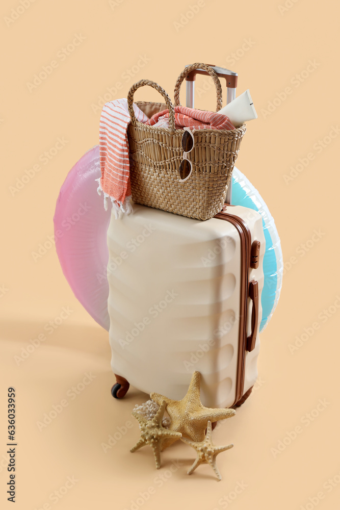 Suitcase with inflatable ring, starfishes and bag full of beach accessories on pale orange backgroun