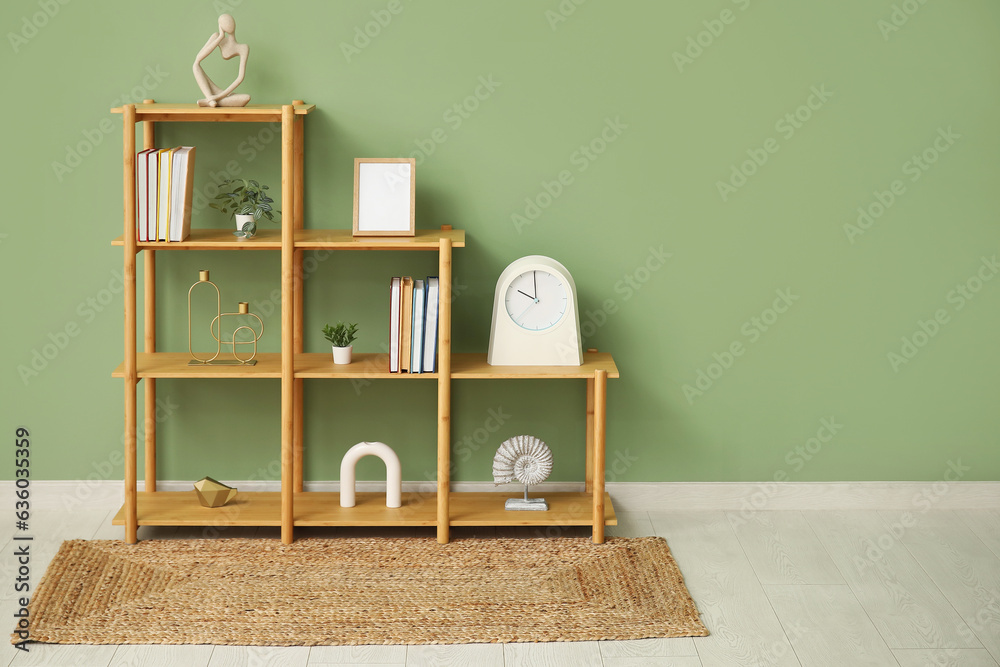 Shelving unit with books, clock and blank frame near green wall in room