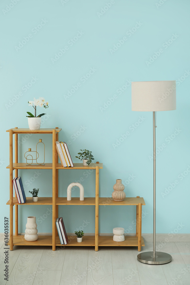 Shelving unit with books, decor and lamp near blue wall in room