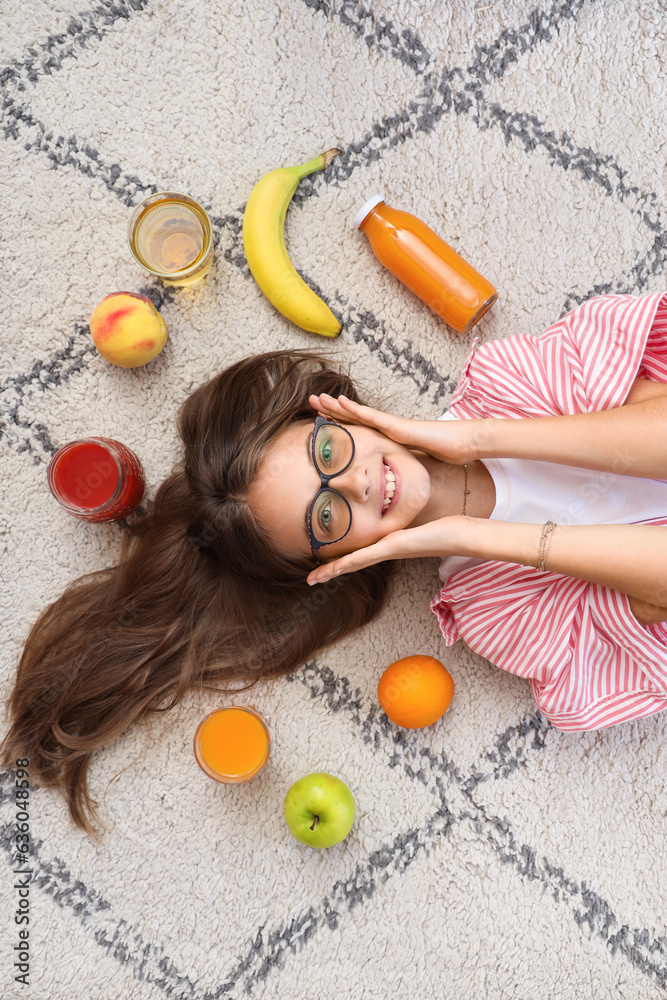 Little girl with juice and fruits lying on carpet, top view