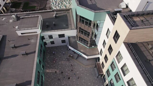 Modern building construction of school yard and rooftop. Students enter new academy premises with ciolourful facade aerial view.