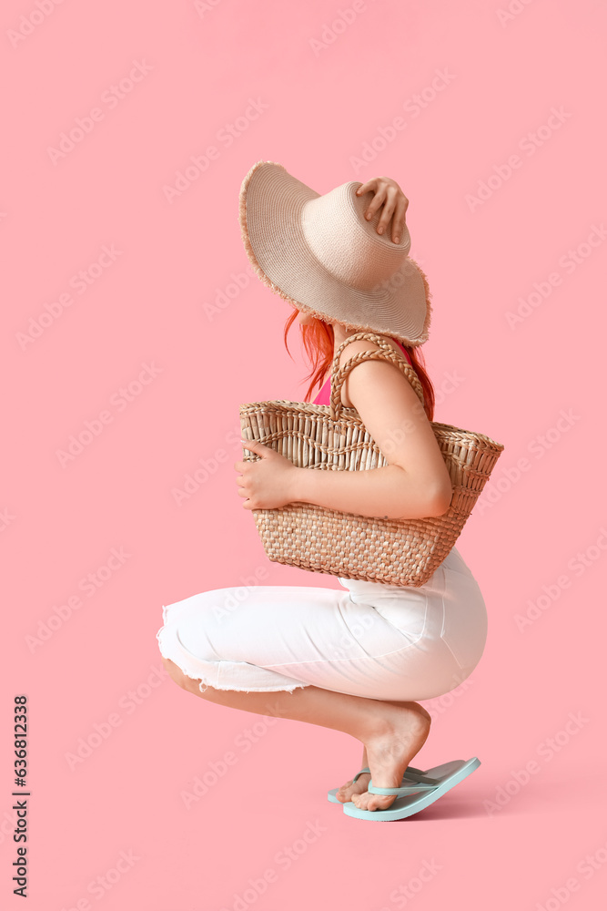 Beautiful young woman in stylish flip flops with beach accessories sitting on pink background