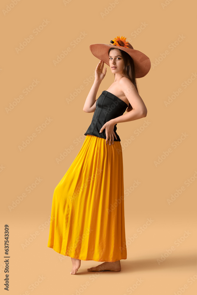 Young woman in wicker hat with beautiful sunflower on orange background