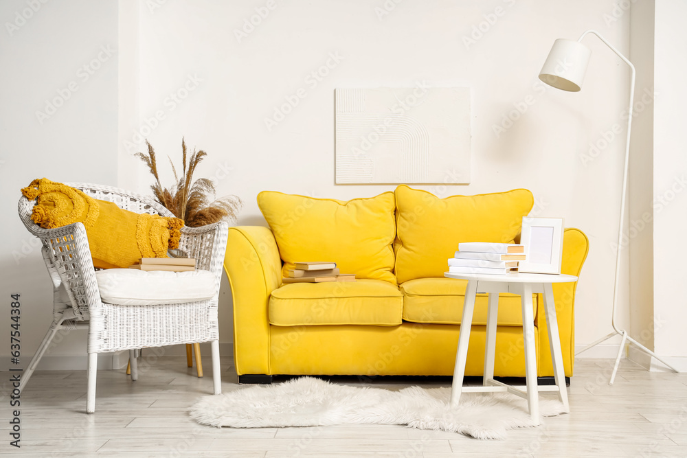 Interior of living room with yellow sofa, armchair and books on table