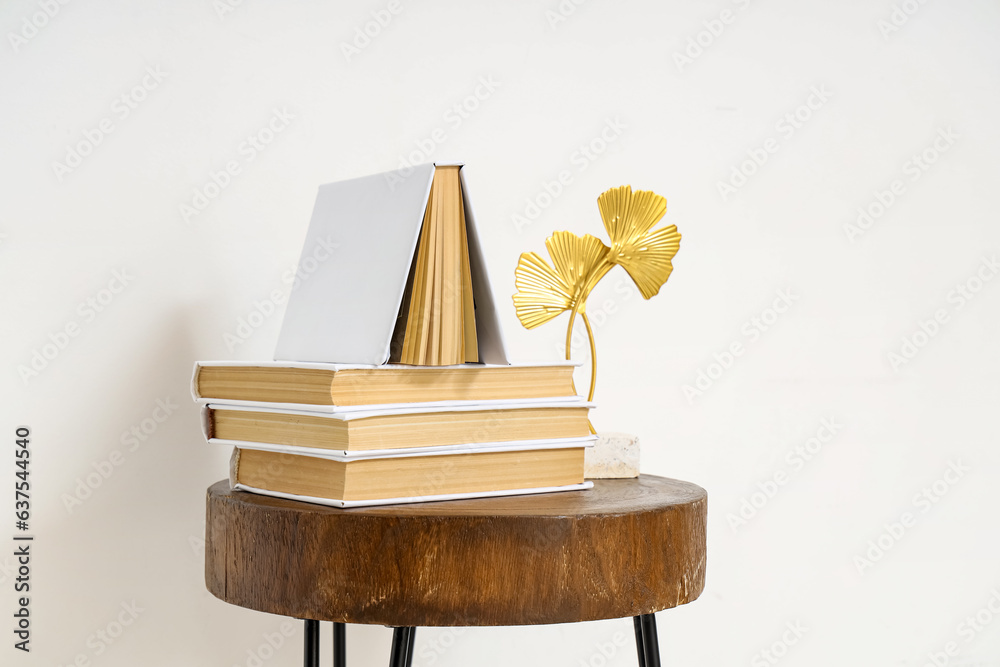 Stack of books with decor on table near light wall