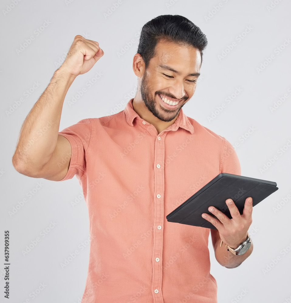 Happy asian man, tablet and fist pump in winning, celebration or promotion against a white studio ba
