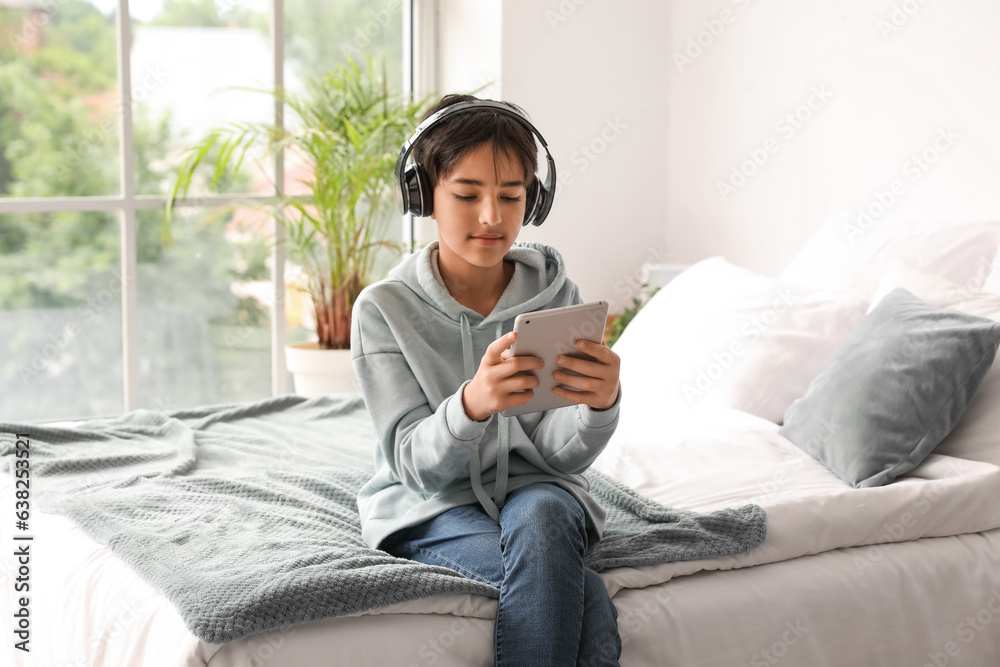 Little boy with headphones using tablet computer in bedroom