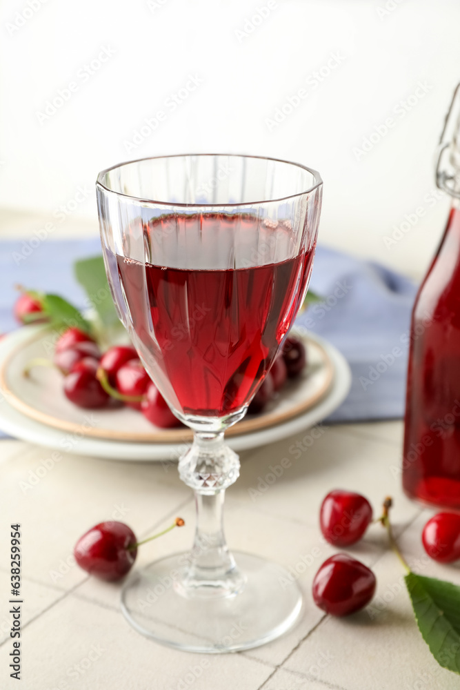 Glass of sweet cherry liqueur with berries on white tile table