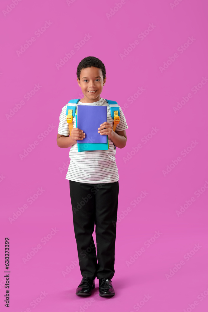 Little African-American schoolboy in stylish uniform with notebooks on purple background