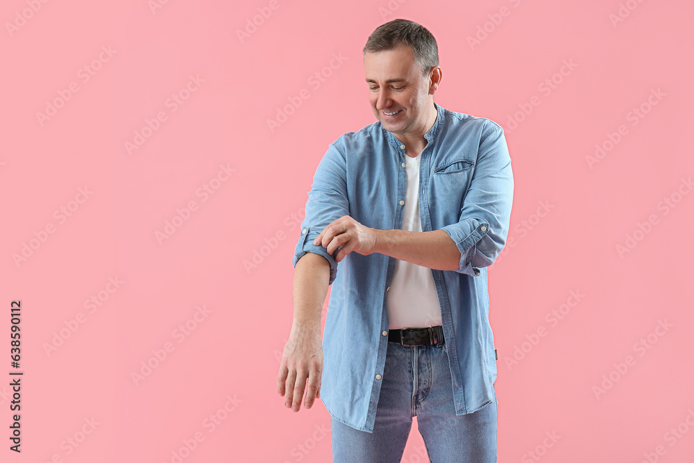 Mature man rolling up his sleeve on pink background