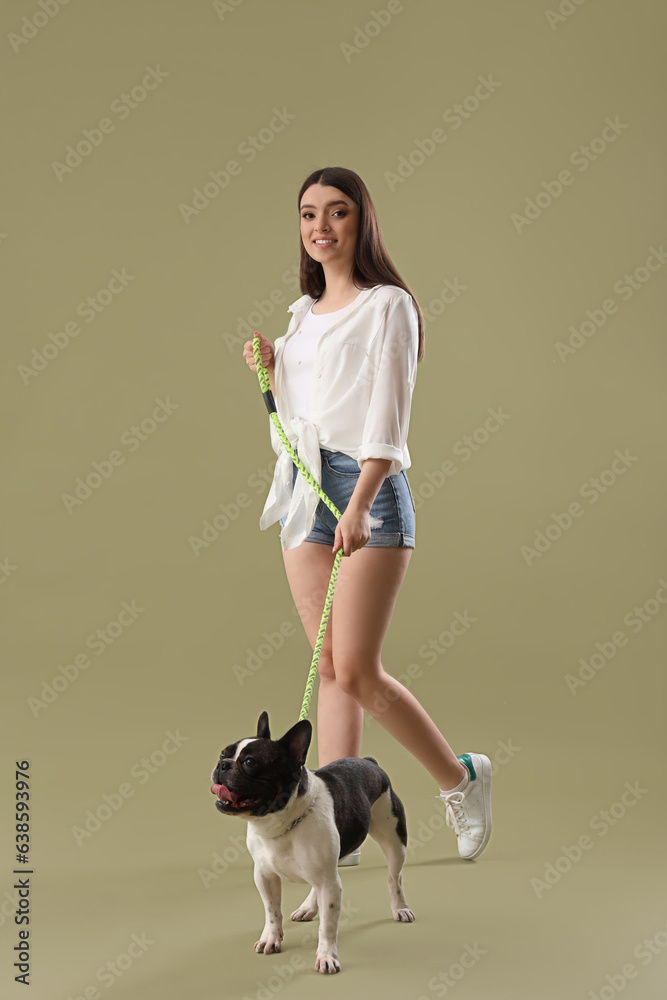 Young woman walking with her French bulldog on green background