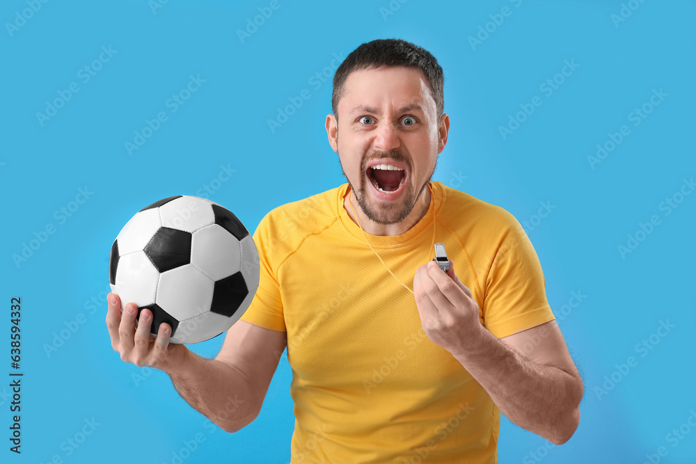 Angry male coach with soccer ball and whistle on blue background