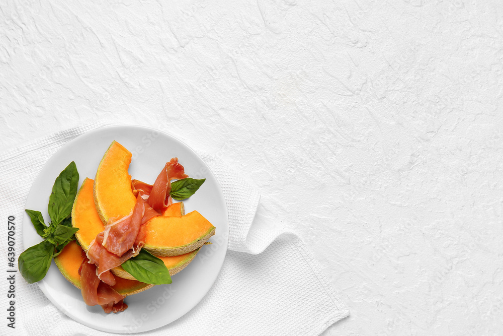 Plate with tasty melon, prosciutto and basil on light background