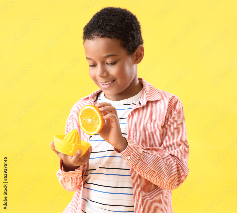 Little African-American boy with slice of orange and juicer on yellow background