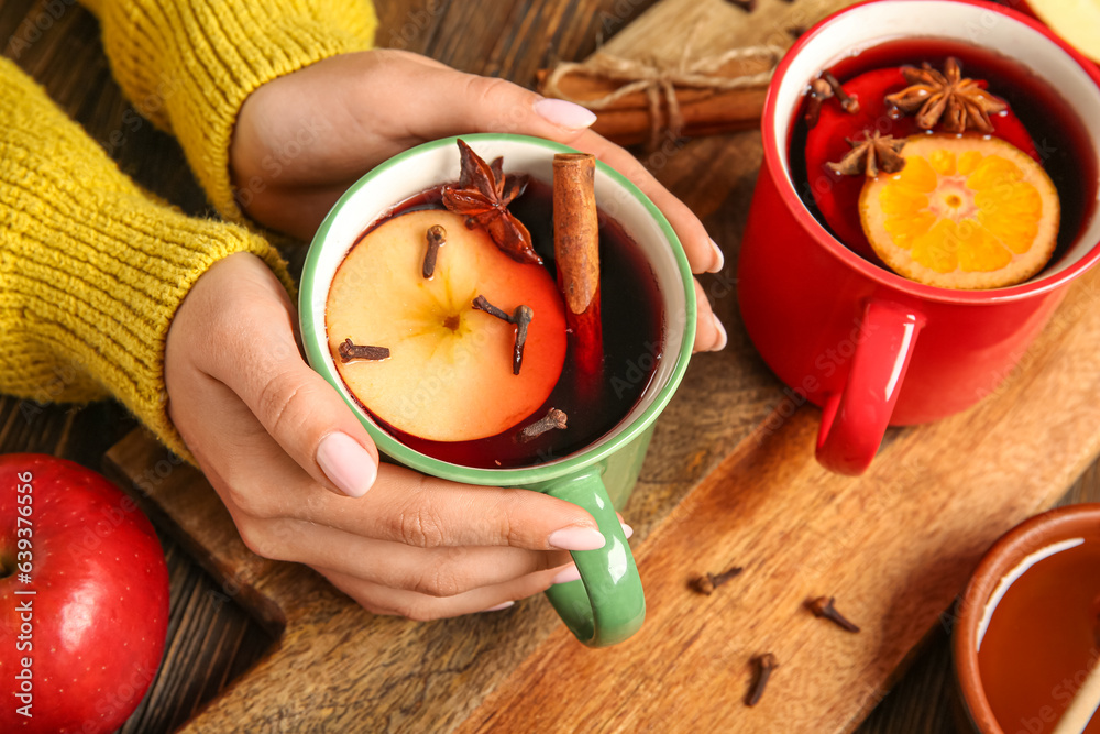 Female hands with cups of hot mulled wine with apple on wooden background