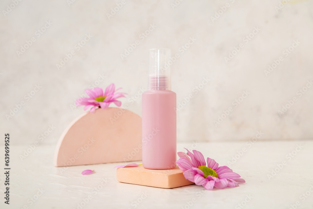 Composition with bottle of cosmetic product, plaster podiums and flowers on light background