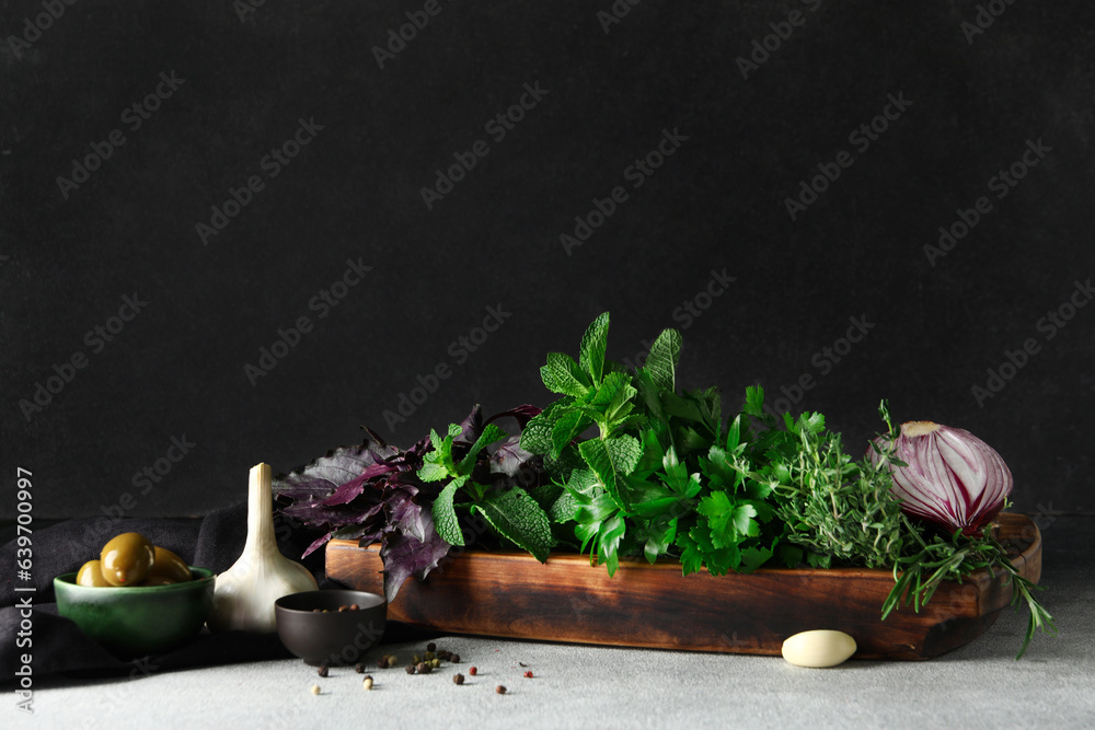 Wooden board with fresh herbs and spices on table against dark background