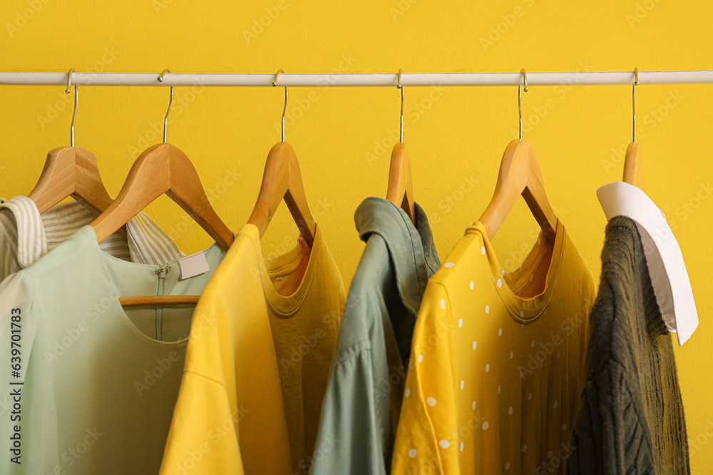 Different clothes hanging on rack against yellow background, closeup