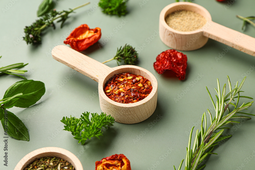 Wooden scoops with spices, dried tomatoes and herbs on color background