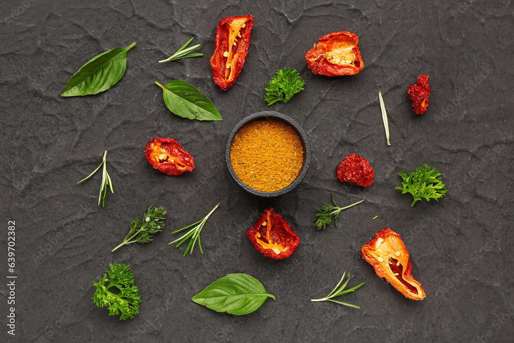 Composition with turmeric powder, dried tomatoes and herbs on dark background