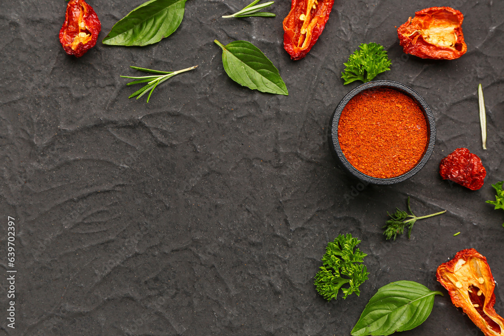 Composition with paprika powder, dried tomatoes and fresh herbs on dark background