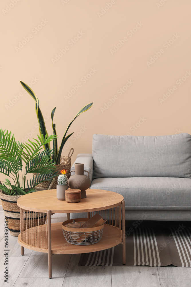 Coffee table with vase, cozy grey sofa and houseplants near beige wall
