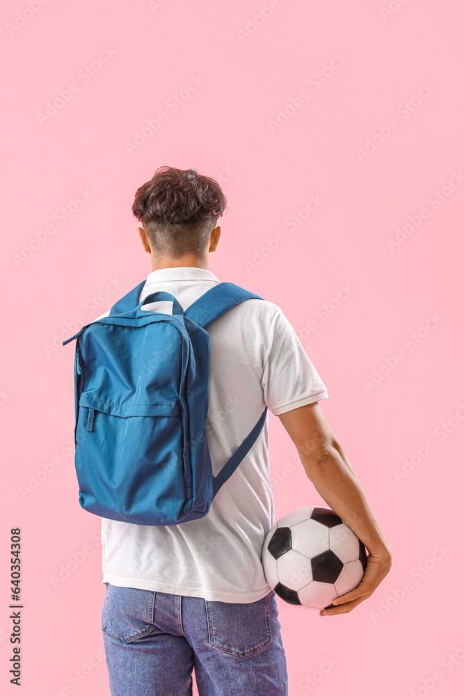 Male student with backpack and soccer ball on pink background, back view