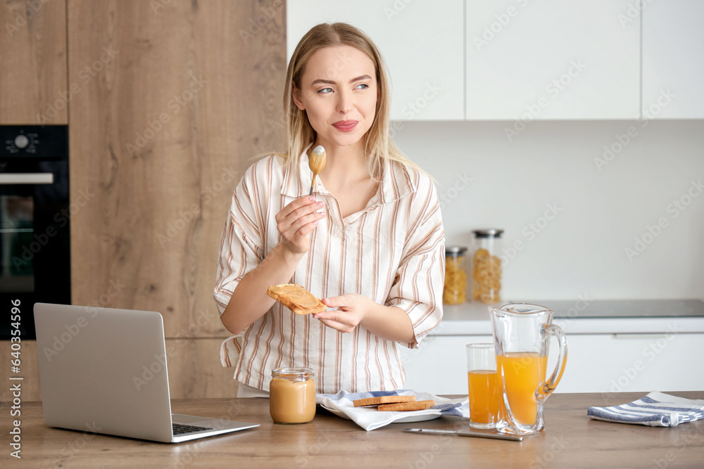 Young woman spreading tasty nut butter onto toast in kitchen