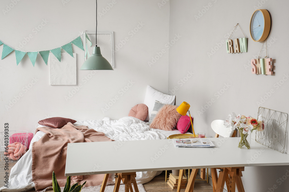 Interior of childrens bedroom with white table, cozy bed and garland