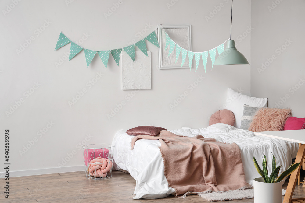 Interior of childrens bedroom with cozy bed, table and garland