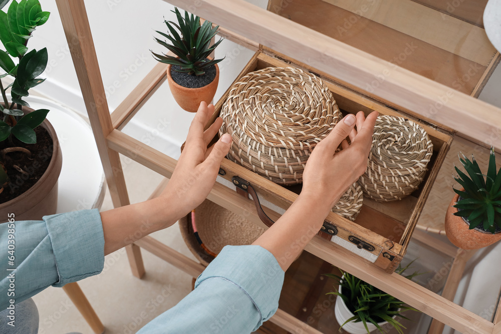 Woman decorating shelving unit with wicker baskets, closeup