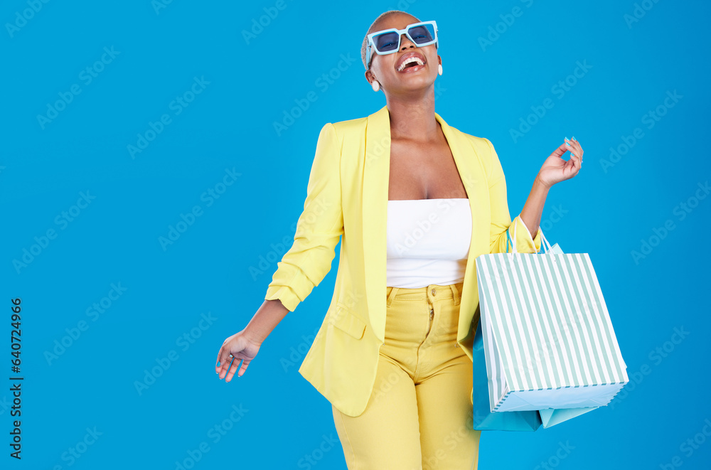 Fashion, deal and black woman in studio with shopping, bag and glasses, excited and smile on blue ba
