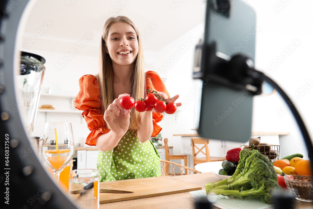 Female blogger with tomatoes recording cooking video in kitchen