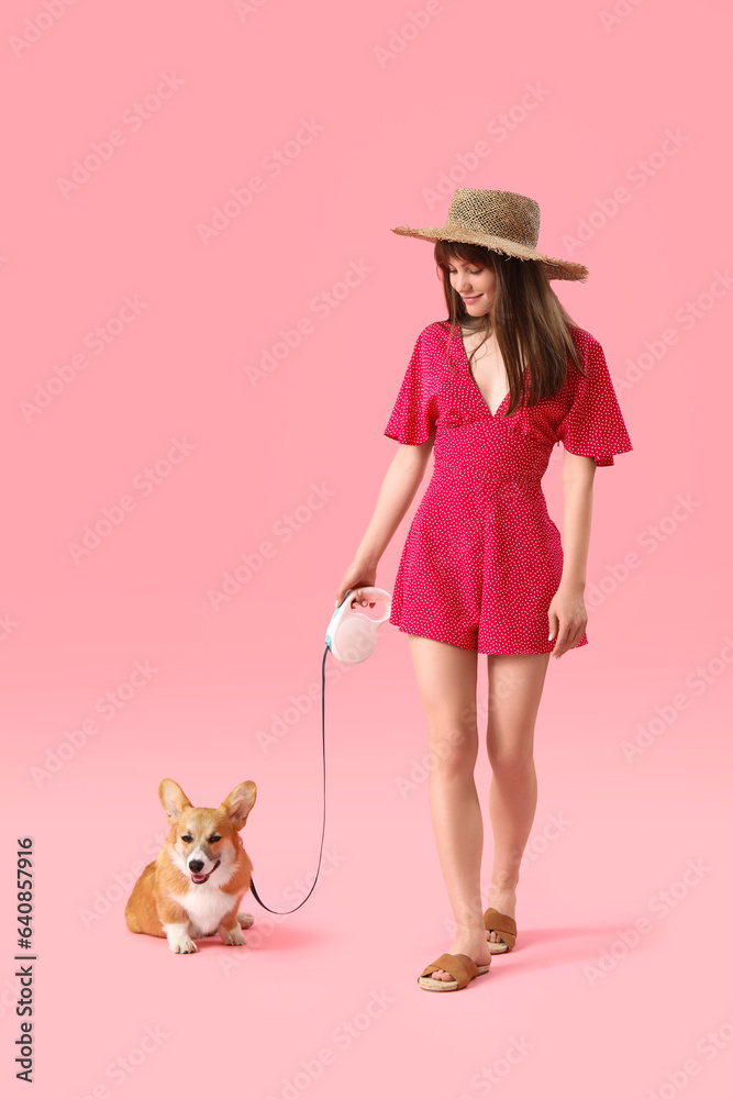 Fashionable young woman taking a walk with cute Corgi dog on pink background