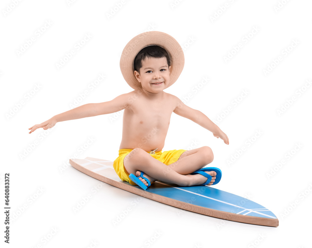 Cute little Asian boy sitting on surfboard against white background