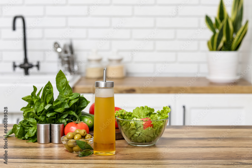 Bottle with oil, olives, vegetables and fresh salad on table in kitchen