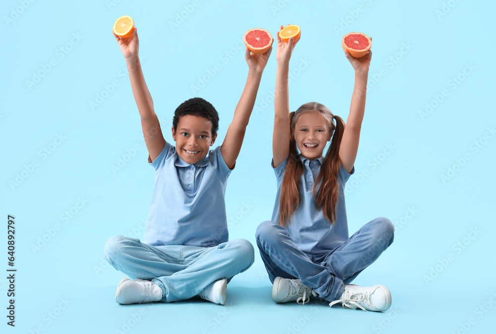 Little children with fresh citruses sitting on blue background