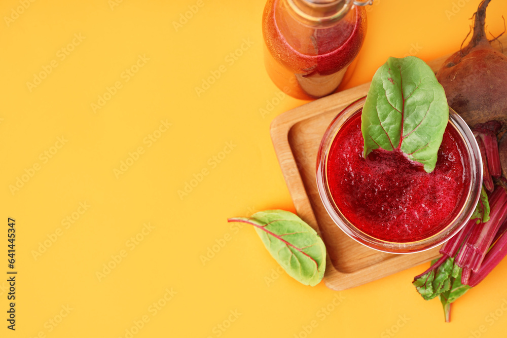 Board with glass and bottle of healthy beet juice on orange background