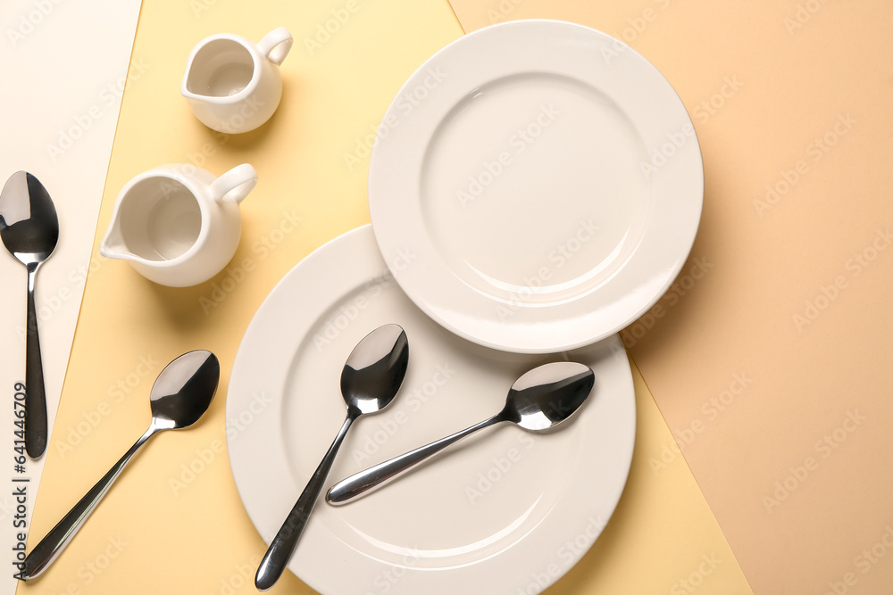 Clean plates, set of spoons and pitchers on beige background