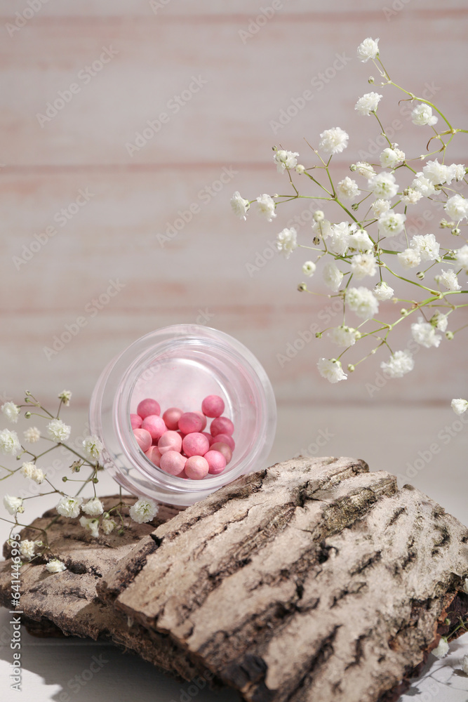 Jar of blush balls, tree bark and gypsophila flowers on light wooden table, closeup