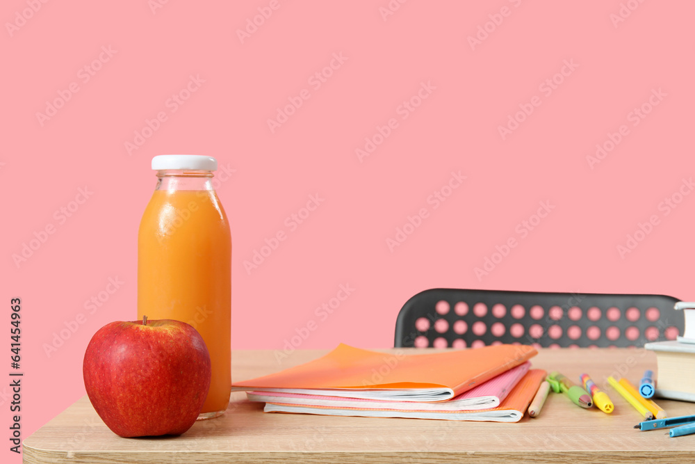 Modern school desk with lunch and stationery on pink background