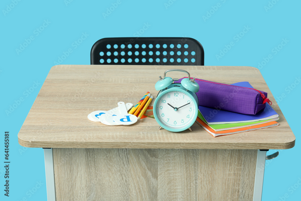 Modern school desk with alarm clock and stationery on blue background