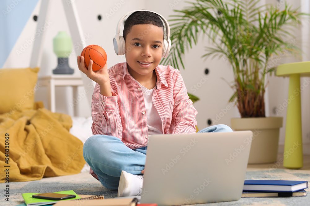 Little African-American boy with ball studying online in bedroom